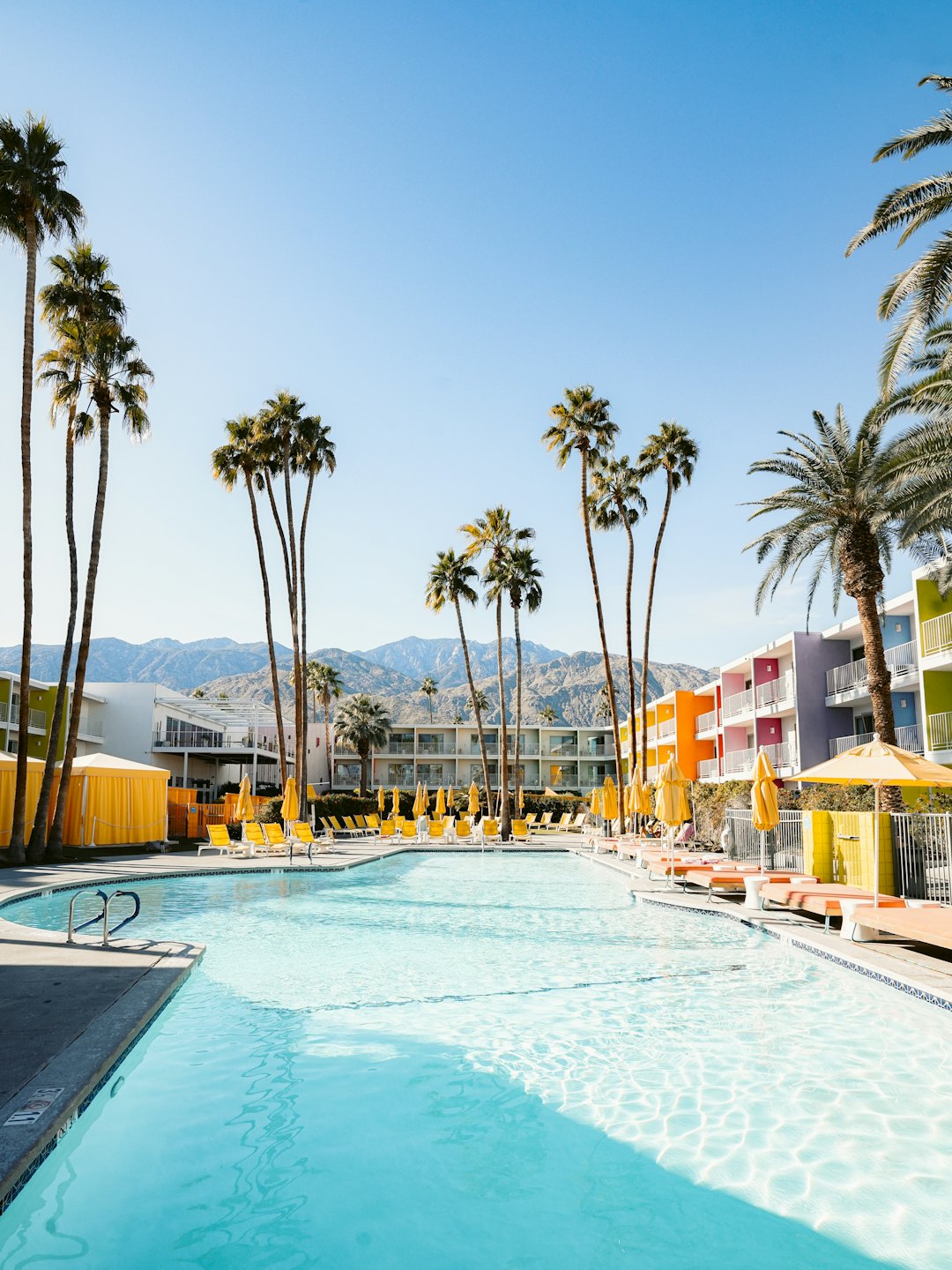 Resort swimming pool area with colorful buildings and palm trees.