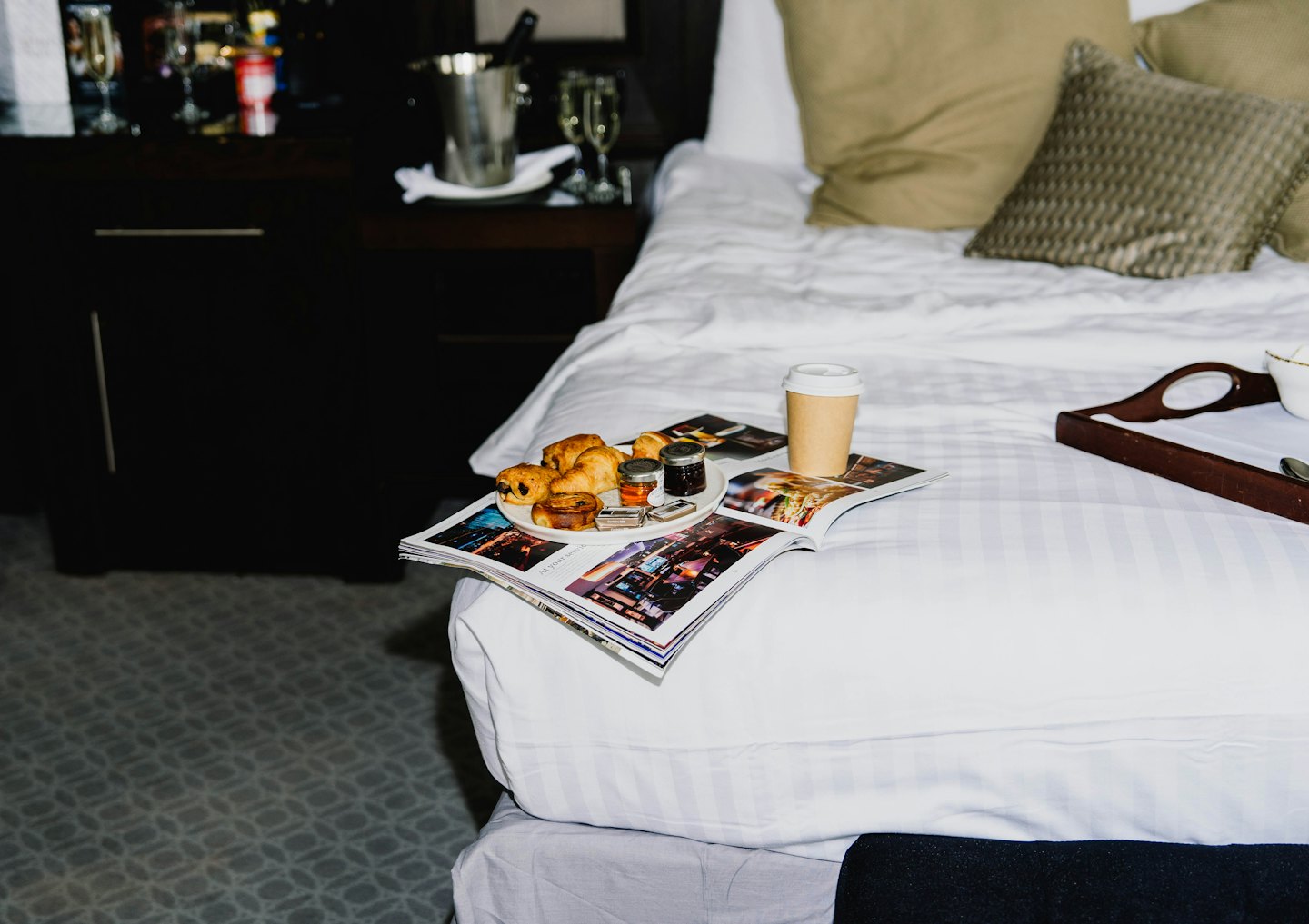 Croissants and coffee on a magazine on a white bed.
