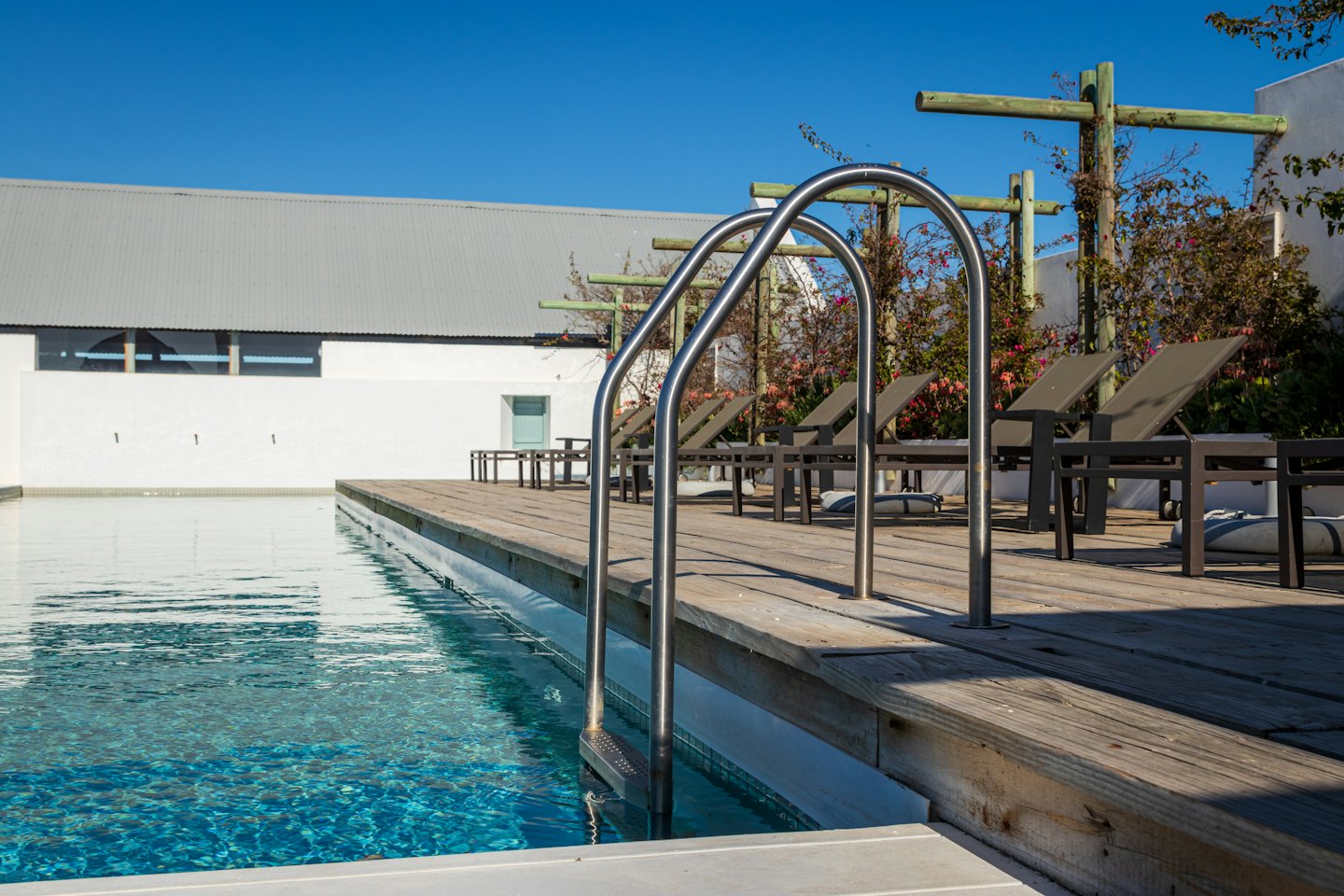 Brown lounge chairs sit on a deck beside a hotel swimming pool.