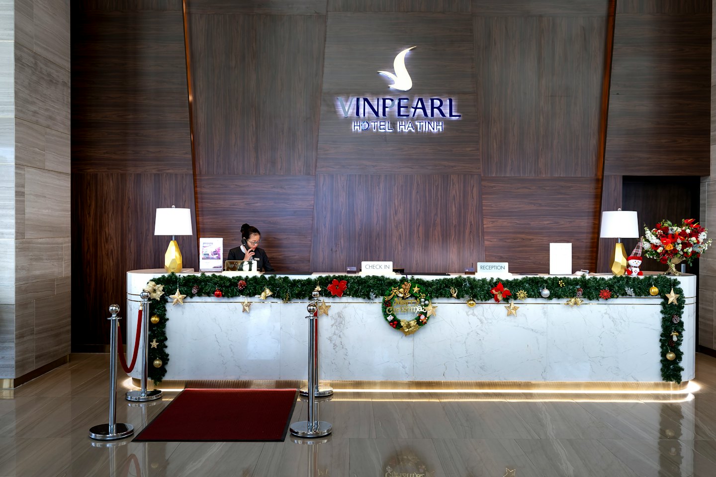 Hotel receptionist talks on the phone at a festive decorated desk.