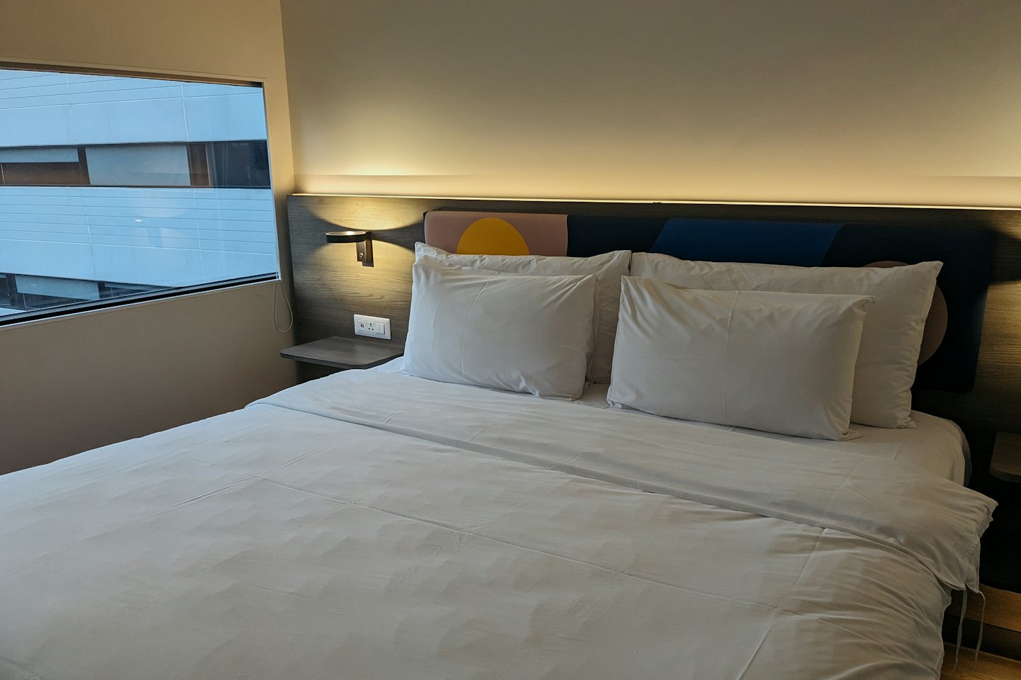 A hotel bed with white linens and a wooden headboard.