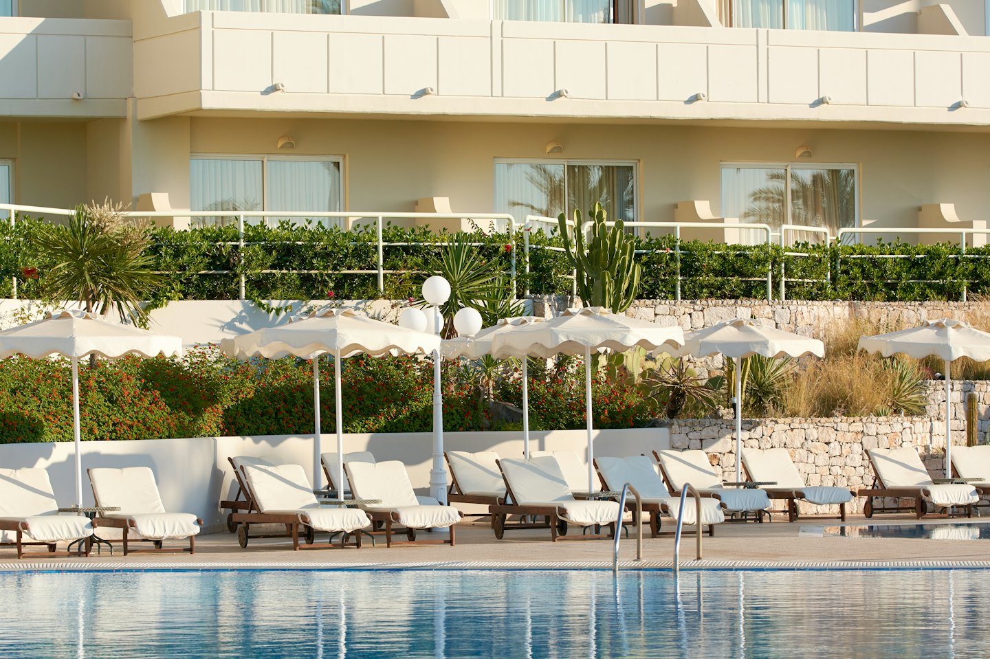 Sun loungers and umbrellas line a resort pool near terraced gardens.