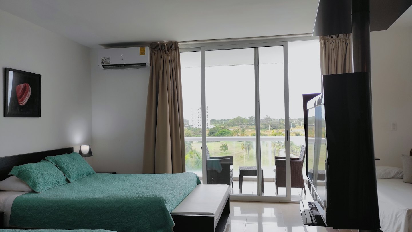 Modern hotel bedroom with balcony views of a green landscape.