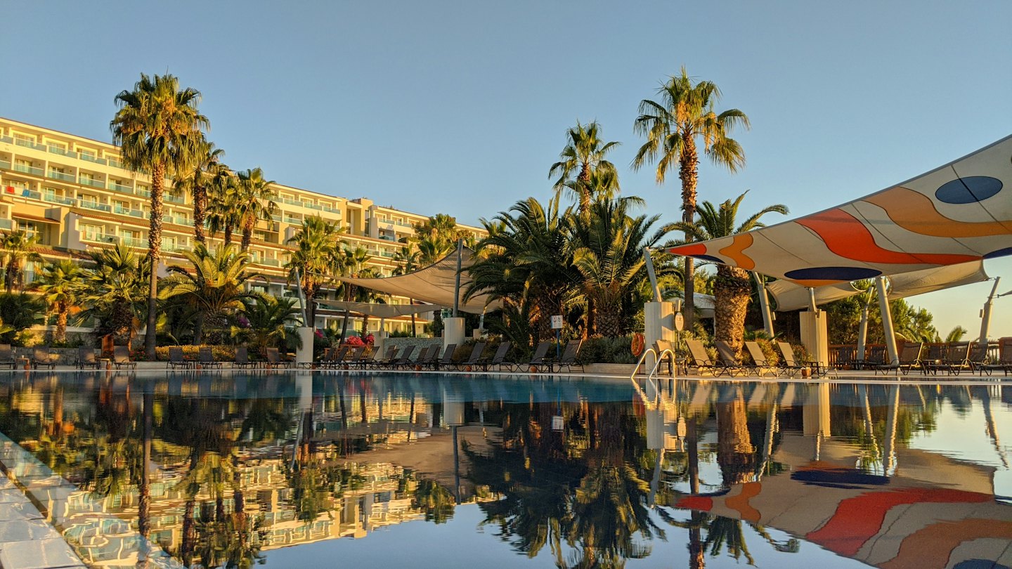 A luxury resort pool reflects the surrounding hotel and palm trees.